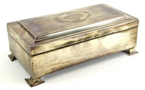 A George V silver cigarette box, the hinged shaped lid with engine turned decoration and with central monogram, within an elaborate cartouche, on ogee feet, Birmingham 1921, 20cm wide, 6.5cm high, 10.5cm deep.