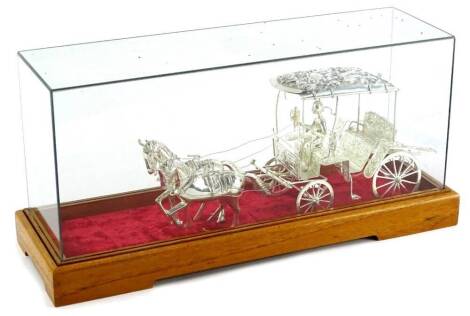 A continental white metal model of a carriage, pulled by two horses, in a glazed case, the case 38cm long.