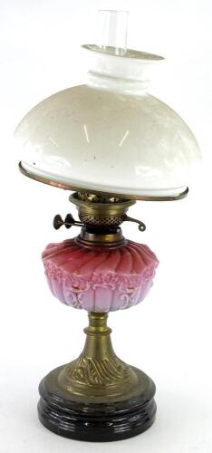 A Victorian brass oil lamp, with white opaque shade, pink tinted reservoir, on a ceramic base, 60cm high overall.