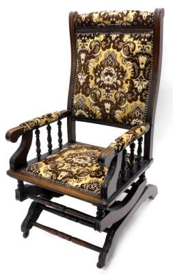 A walnut rocking chair, with a padded back, arm rests and seat, upholstered in brown and gold fabric, with shaped sprung rockers, possibly American.