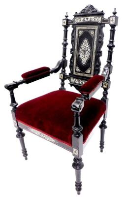 A late Victorian ebonised and ivory inlaid open armchair, the panelled back decorated with scrolls, geometric devices, etc., on turned supports, with velvet padded seat and arm rests, on turned tapering legs.