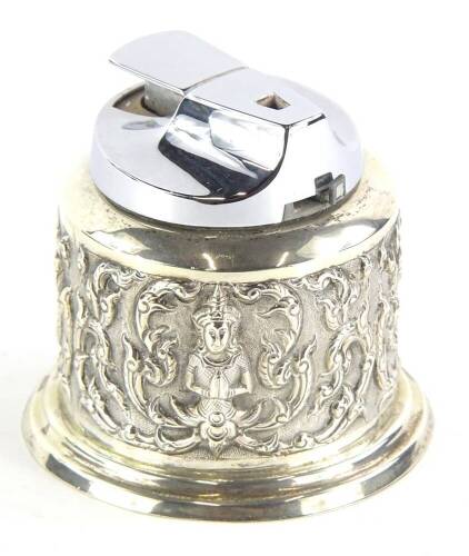 A white metal Eastern table lighter, of cylindrical form, with removable chrome insert, heavily repousse decorated with elephant heads and scrolls, on a plain circular foot, marked Sterling beneath, 9cm high, 8oz all in.