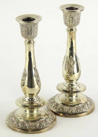 A pair of white metal candlesticks, each with geometric dish holders, baluster stems and stepped bases raised with a floral banding, marked 925 beneath, 21cm high (2, weighted).