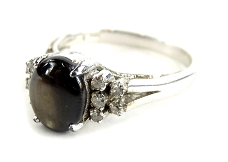 A dress ring, set with opalescent style oval black stone, with tiered white stone set shoulders, on V splayed and scroll motif, white metal marked 14K, ring size U½, 5.4g all in, boxed.