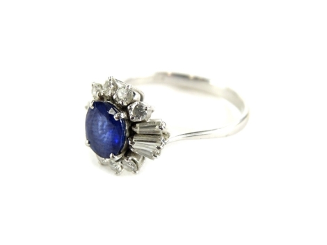 An 18ct white gold sapphire and diamond cluster ring, with oval cut dark blue sapphire, 7.4mm x 6.8mm x 3mm, surrounded by eight round brilliant cut tiny diamonds and six baguette cut diamonds, in basket claw setting, ring size R½, 4.7g all in, boxed.