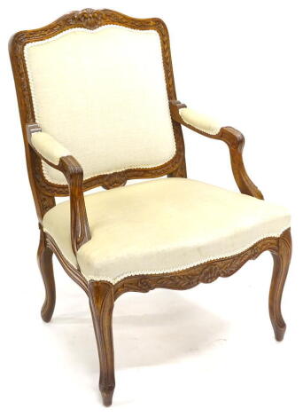 A French style walnut open armchair, upholstered in beige fabric to the back, arm rests and seat, on cabriole legs, possibly American. The upholstery in this lot does not comply with the 1988 (Fire & Fire Furnishing) Regulations, unless sold to a known ex