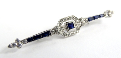 An Art Deco sapphire & diamond bar brooch, set with central square cut blue sapphire 3mm x 3mm, surrounded by twenty four round brilliant cut diamonds, and with a further four diamonds to each end, each approx 1mm diameter, totalling approx 0.15cts overal