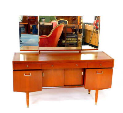 A Nathan teak dressing table, with a triptych mirror, over one long and two short drawers, above a pair of central sliding doors, flanked by cupboard doors, raised on cylindrical legs, on brass capped feet, 70cm high, 137cm wide, 45.5cm deep.