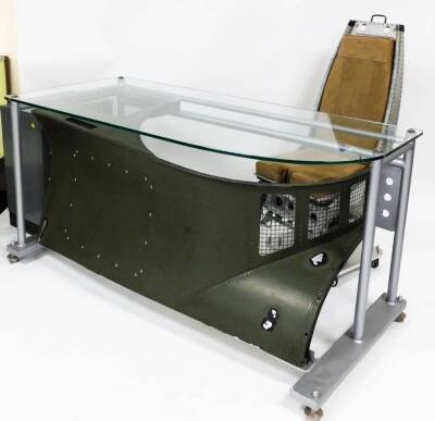 An unusual scratch built Lynx helicopter desk, comprised of Lynx helicopter parts, the wing shaped glass top, raised above a studded helicopter section on a platform base, terminating in compressed feet, 84cm high, 164cm wide, 69cm deep, together with a o - 2