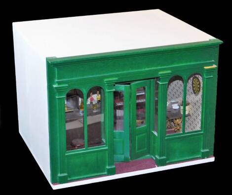 A 20th model tavern bar, with articulated front painted green, the white body with open section and various removable miniature items, pub table, bar, bottles, etc., the main body 30cm high, 38cm wide, 31cm deep.