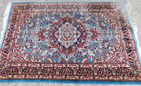 A Turkish style rug, with a central cartouche shaped medallion in red and navy on a pale blue ground, with one wide and two narrow borders, with fringes to end, 186cm x 117cm.