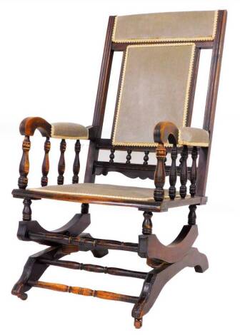 A late 19thC rocking chair, with overstuffed back, arms and serpentine seat, on a scroll base, fronted by turned horizontal supports, 100cm high.