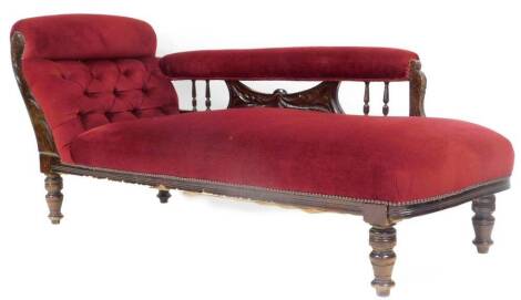 An Edwardian walnut stained chaise lounge, in later part studded burgundy material re upholstered in 1988 with a shaped spindle back on turned legs with scroll end, 74cm high, 174cm wide, 67cm deep.