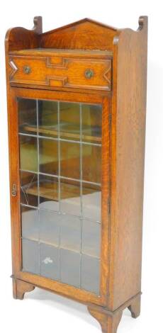 An early 20thC oak cabinet, the triangular cornice raised above carved drawer and astragal glazed door revealing plain shelves, on stylized bracket feet, 138cm high, 59cm wide, 26cm deep.