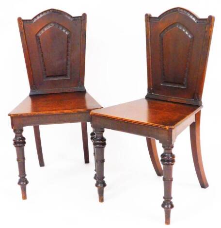 A pair of 19thC oak hall chairs, each with shaped partially carved backs, canted seats and turned front and back sabre legs, 93cm high. (2)