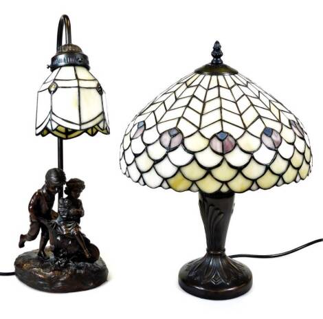 A Tiffany style lamp, with shaped shade predominantly in white and blue, 46cm high, and a further table lamp with similar shade set with figures. (2)