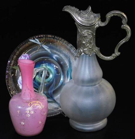 A frosted glass claret jug, with plated mount, 28cm high, an early 20thC pink and clear glass ewer, painted with a floral scene and a glass plate decorated with dragonfly and flowers, on a textured ground. (3)