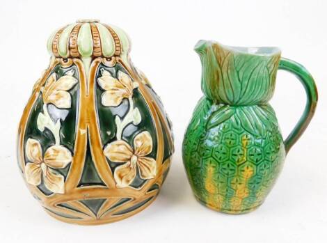 An early 20thC Majolica jug, in a green and yellow floral pattern with plain beak spout and handle, 18cm high, and a Majolica pottery shade raised with flowers, with compressed top. (2)