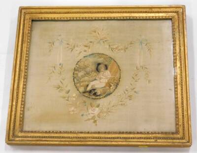 An early 19thC silk embroidered picture, decorated centrally with a young boy, sheep, etc., surrounded by a floral cartouche, embellished with ribbons, wheat ears, etc., 34.5cm x 42cm.