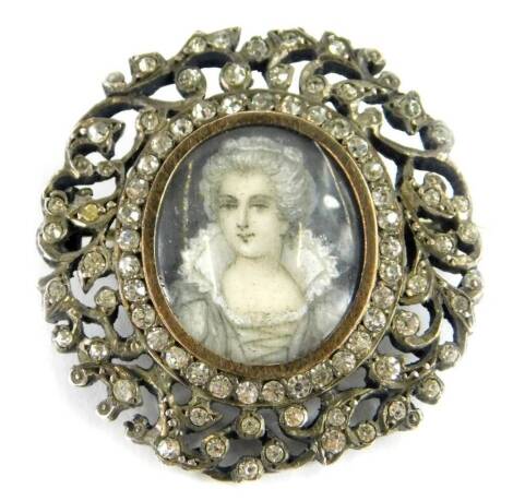 A Victorian paste stone set portrait brooch, with central oval portrait panel of a lady in Victorian dress, with a silver gilt gold coloured border, surrounded by paste stones within a pierced scroll design outer border, with white metal back, with single