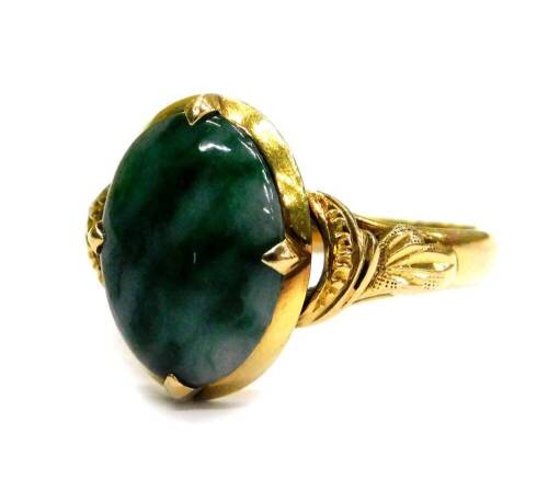 A modern jade set dress ring, the oval jade with pale and dark green striations, in a four claw setting, in a yellow metal frame, with fanned and etched design shoulders, ring size M½, 4.3g all in.