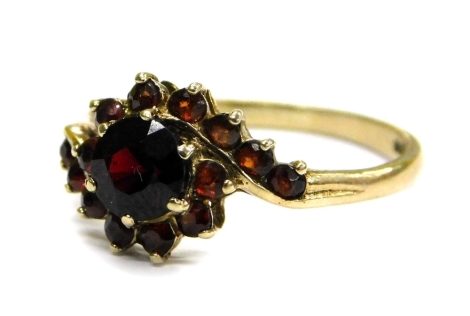 A 9ct gold garnet set dress ring, of twist design with large central stone, flanked by smaller stone on single row twist design, ring size N, 1.7g all in.