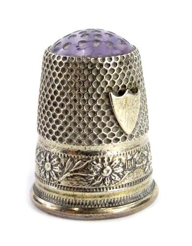 A small white metal thimble, engraved and cast with flower heads, vacant cartouche and with a purple enamel end. Provenance: The Estate of Miss Rachel Monson.