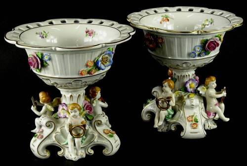 A pair of Schierholz porcelain centrepieces, each with flower encrusted decoration and with a trefoil shaped base, each applied with putti musicians, 20cm high.