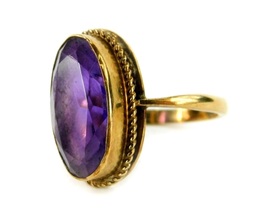 A 9ct gold dress ring, set with oval faceted amethyst stone, in rub over gold setting, with rope twist design border, ring size L½, 3.1g all in.