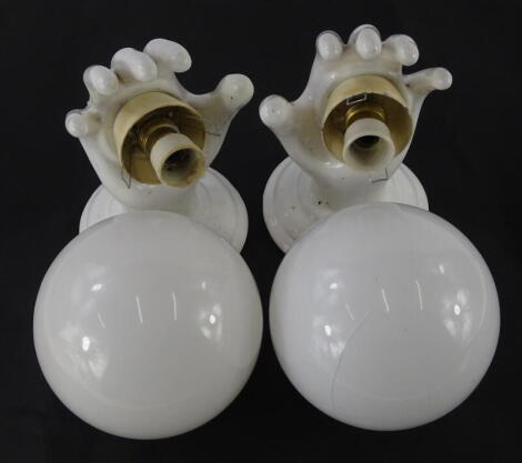 An unusual pair of ceramic wall lights, each modelled in the form of a hand, with opaque globe shaped shades.