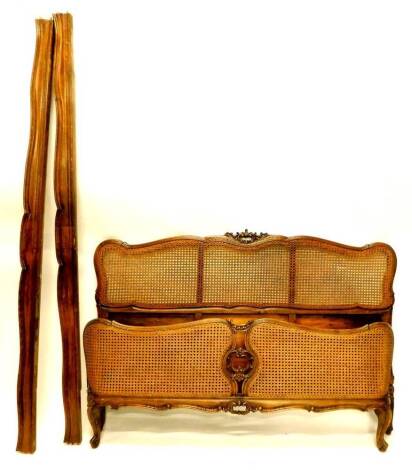 An early 20thC French beech and caned bergere bed head and foot, with a moulded frame carved with flowers, scrolls, etc., 156cm wide.