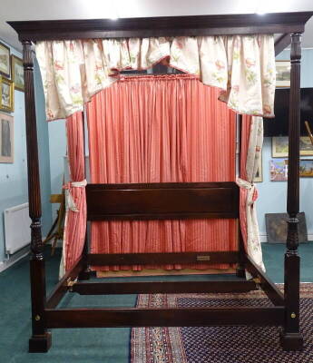 A mahogany four post bed in George III style, with panelled head board, the front posts with reeded carved decoration, sold with floral and pink striped drapes, 247cm high, 205cm wide, 220cm deep.