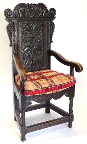 A 19thC and earlier oak Wainscot chair, the panelled back carved with leaves, flowers, scrolls, etc, with shaped arms on turned supports.