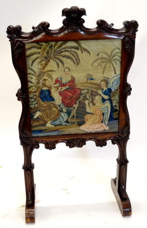 An early Victorian rosewood fire screen, rectangular cartouche shaped frame, carved with a fleur-de-lis scroll, etc. the wool work banner depicting a biblical scene with Jesus, Mary, Joseph and the Angels, etc. on end supports, 107cm x 60cm.