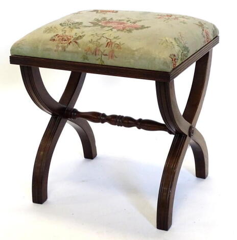 A mahogany stool in Regency style, with a padded top, reeded edge, on X shaped end supports with turn stretcher 42cm wide. The upholstery in this lot does not comply with the 1988 (Fire & Fire Furnishing) Regulations, unless sold to a known exporter or 