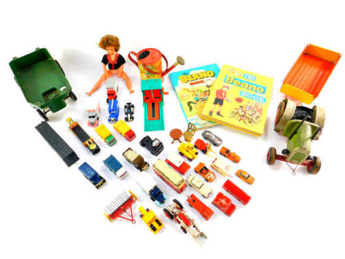 A mid 20thC tin plate red and yellow trailer, carved and painted ribbon tractor, and a green plastic trailer, together with children's annuals, die cast vehicles, child's watering can and a doll. (a quantity)