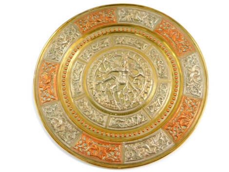 An Indian brass and damascene circular dish, embossed with a Hindu deity surrounded by panels of panels of flowers and scrolling leaves, in white metal and copper, 33cm diameter.