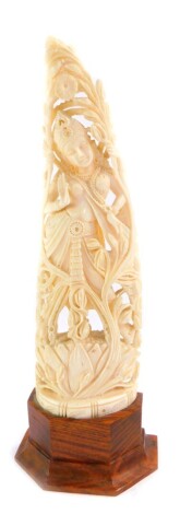 An Indian ivory carving of Shiva, modelled standing on a lotus flower, with flowering around her, raised on a hexagonal demi lune wooden base, 26cm high.