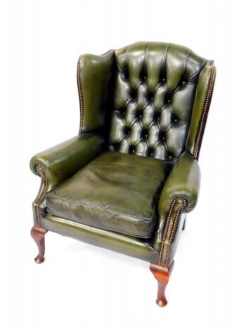 An oak and green leather button back wing armchair, raised on cabriole legs.