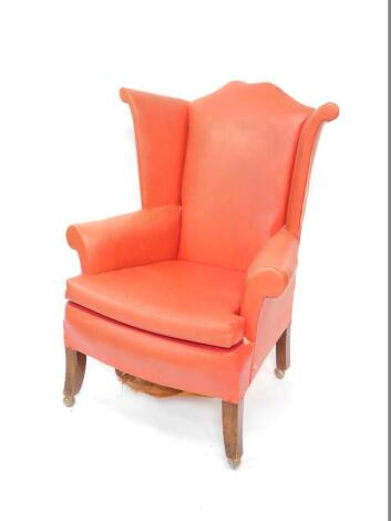 A mid 20thC oak framed wing back armchair, upholstered in red leatherette, raised on outswept legs on castors.