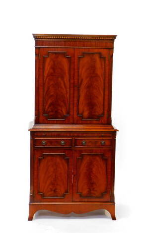 A Georgian style mahogany drinks cabinet, the dentil moulded pediment over two doors, opening to reveal one wooden and one glass shelf, over a slide, two drawers and two cupboard doors opening to reveal three recesses, raised on splayed feet, 166cm high, 