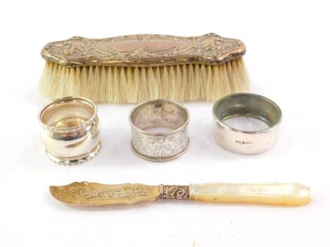 An Edward VII Art Nouveau silver backed clothes brush, Birmingham 1905, two silver napkin rings, silver and glass lid, Birmingham 1912 and a Victorian silver butter knife with mother of pearl handle, Birmingham 1853, 6.99oz all in.