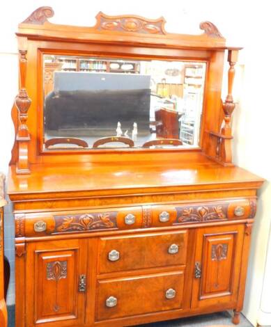 A Victorian walnut mirror back sideboard, with an Art Nouveau fall, carved pediment, above a shelf over two turned and carved columns and rectangular mirrored back inset bevelled glass, over two cushion drawers above two central drawers flanked by cupboar