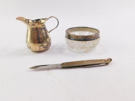 An Edward VII silver miniature cream jug, Birmingham 1905, 0.72oz, cut glass salt with silver mount, Birmingham 1902, and a silver backed folding pocket knife with engine turned decoration, rectangular reserve, presentation engraved, Birmingham 1967.