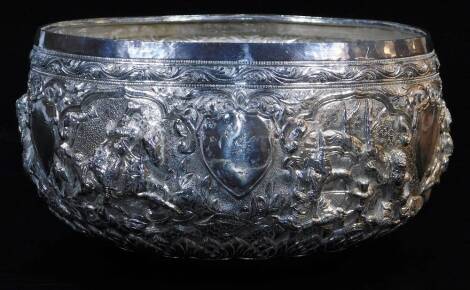 An early 20thC Indian ceremonial bowl, heavily repousse decorated with figures scrolls and flowers, with further hammered decoration, on a plain base, Indian white metal, unmarked 12cm high, 20cm diameter.