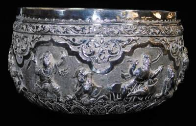 An early 20thC Indian ceremonial bowl, heavily repousse decorated with figures scrolls and flowers, with further hammered decoration, on a plain base, Indian white metal, unmarked, 8cm high, 15cm diameter.