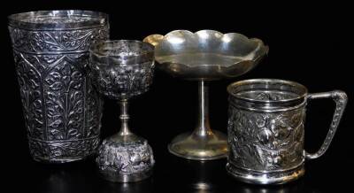 An early 20thC mug, of cylindrical form, heavily decorated with flower heads, 7cm high, an early 20thC Indian footed dish, beaker, etc., Indian metal, unmarked. (a quantity)