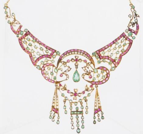 An early to mid 20thC Indian necklace, set with layers of semi precious stones, comprising seed pearls, rubies and emeralds, all rough cut and pale in colour, with elaborate scroll design centre, and three strand tassle drop, in yellow metal setting, on f