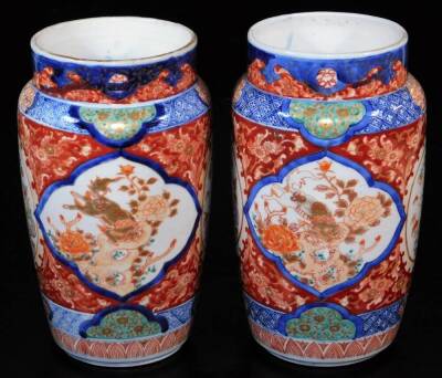 A pair of Imari porcelain vases, each of shouldered cylindrical form decorated with panels of shishi with gilt highlights, further panels of flowers with an upper blue and white geometric border, with panels of flowers, unmarked, 25cm high. (2) - 3