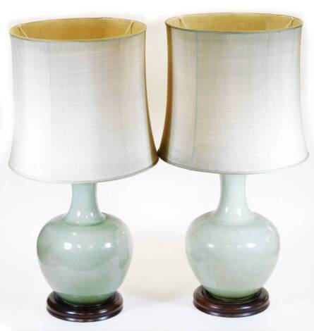 A pair of Chinese celadon porcelain lamp vases, each of bellied circular form with wooden plinths and bases with shades and modern electrical fittings, 84cm high. (2)